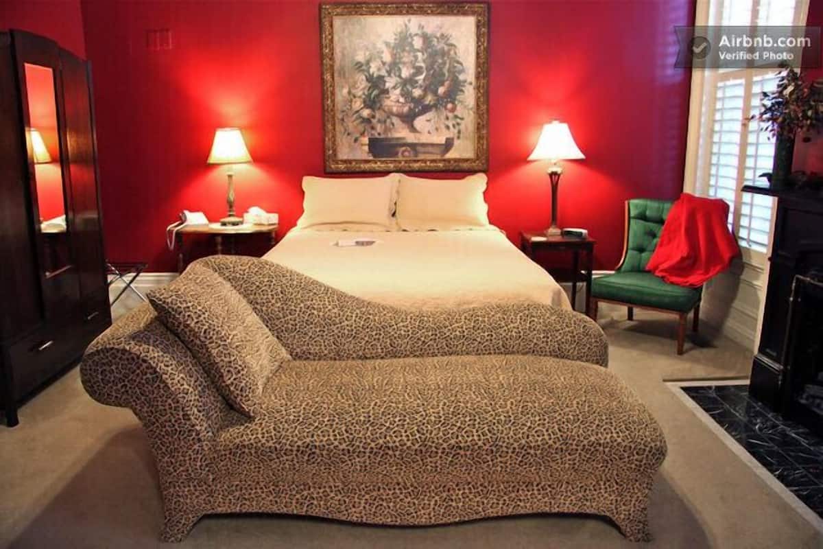 A bedroom with a large bed, two bedside tables, a green chair, and a painting on the wall.