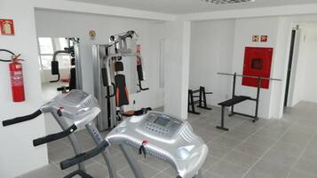 Un gimnasio con cintas de correr, máquinas de pesas y un extintor rojo en la pared.