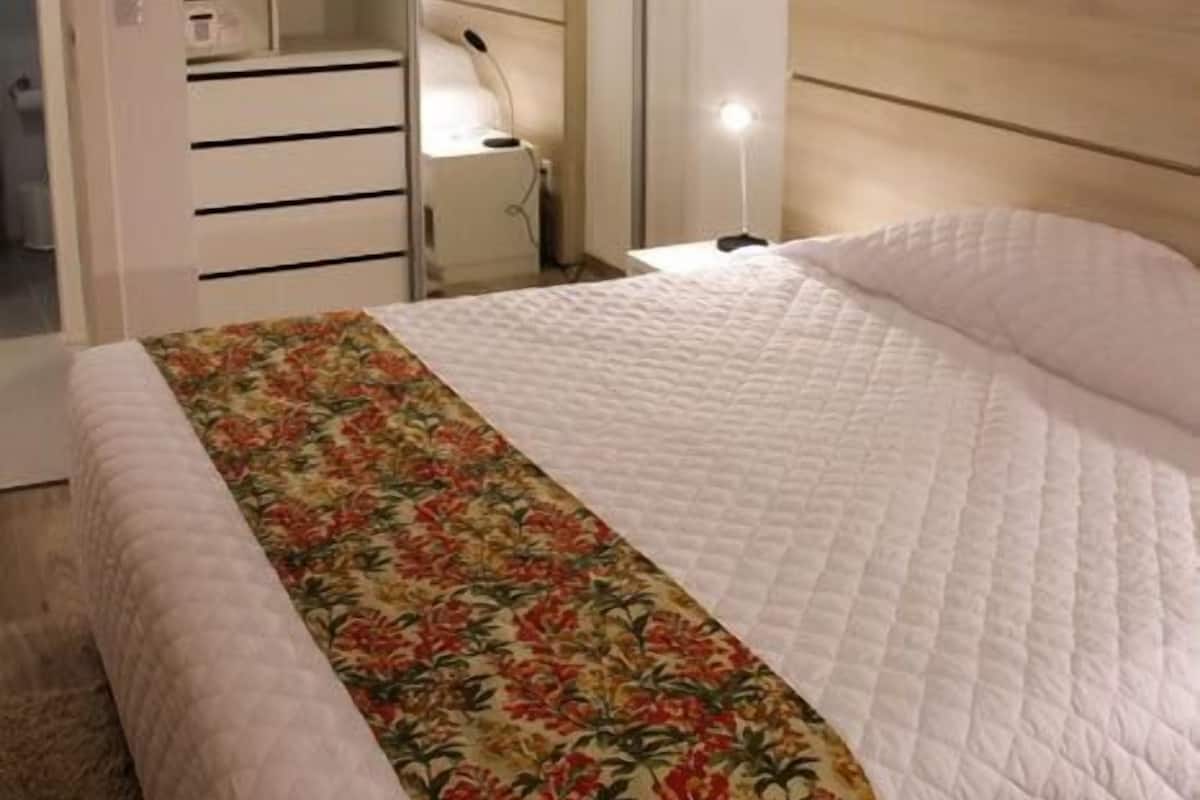 Quarto com uma cama grande, cabeceira de madeira, abajur e guarda-roupa com portas de correr.
