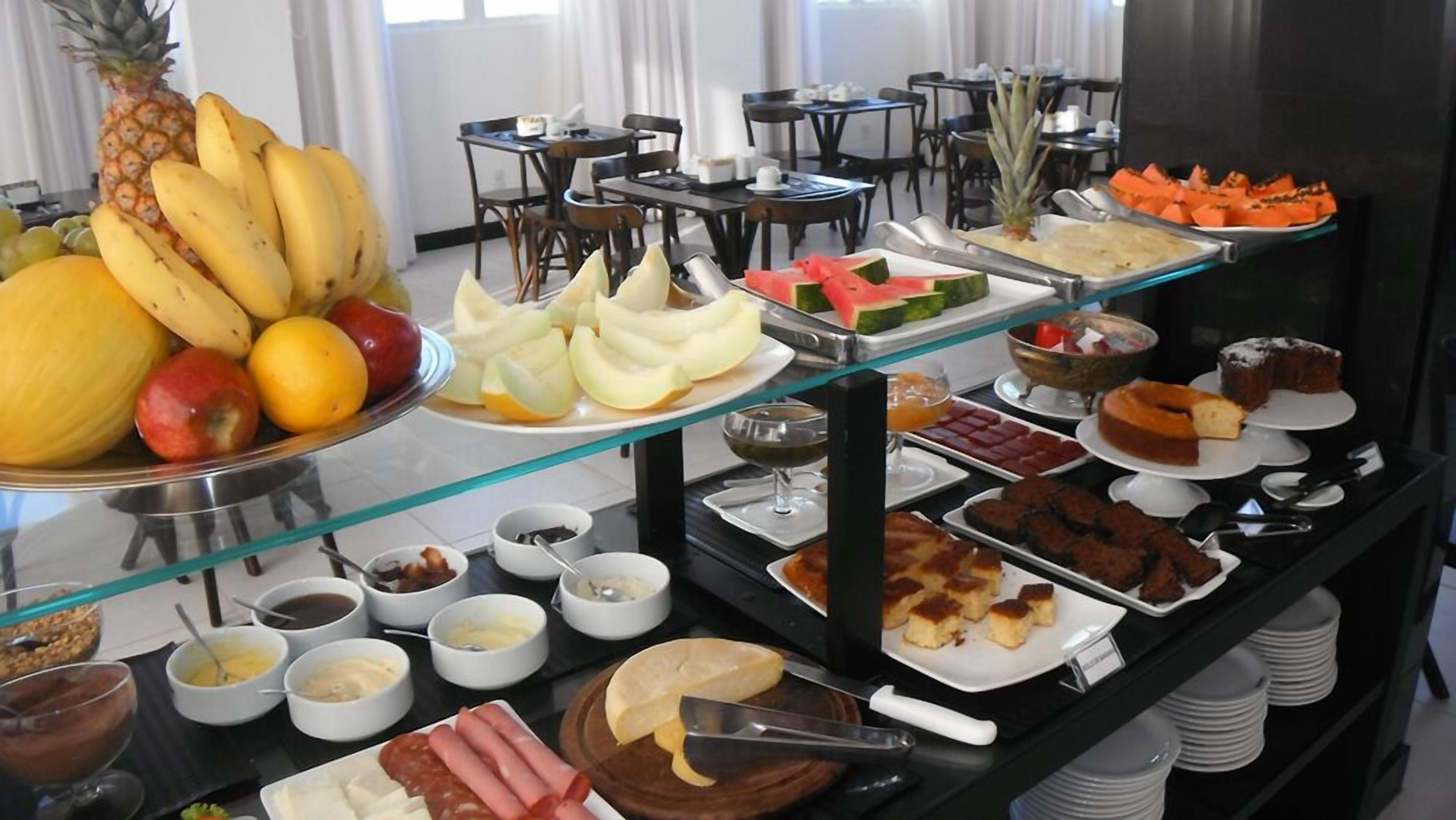 Buffet com diversos alimentos, incluindo frutas, queijos, carnes e sobremesas.