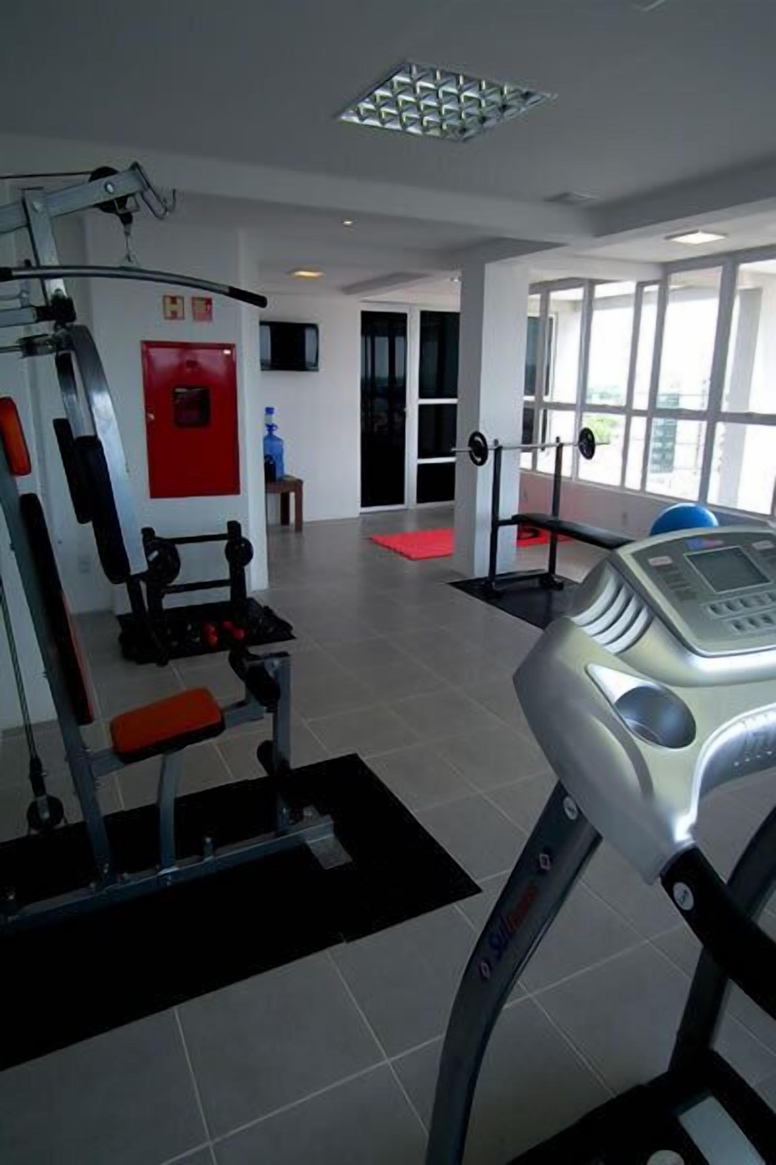 Un gimnasio con equipo de ejercicio, una pared roja y un ventanal grande.