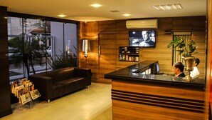 Un área de recepción con un mostrador de madera, un sofá de cuero negro, un televisor montado en la pared y un ventanal con vistas a la calle.