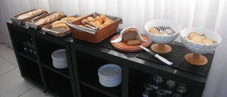 A buffet setup with bread, pastries, and condiments.