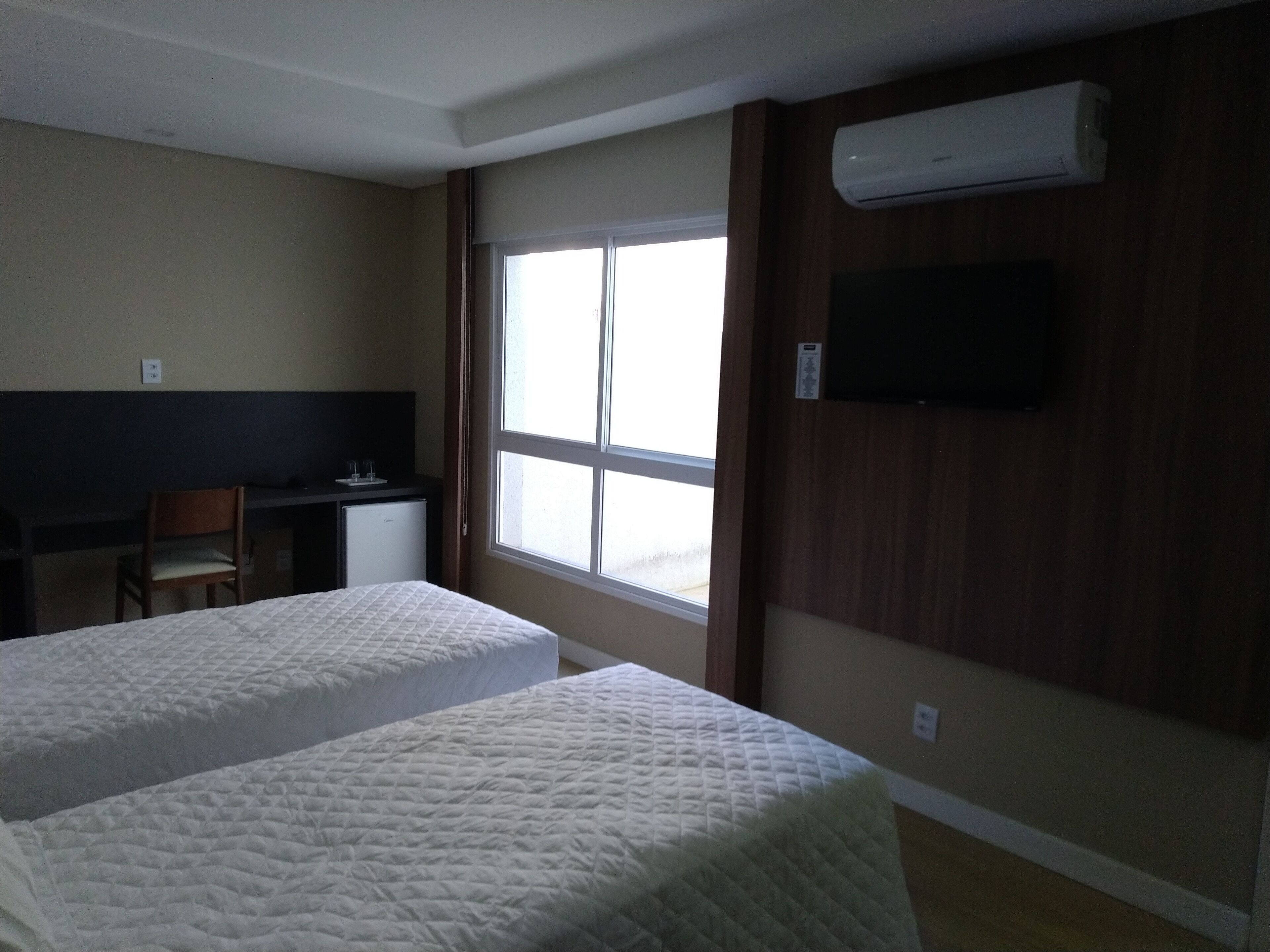 A hotel room with two beds, a desk, a chair, and a TV mounted on the wall.