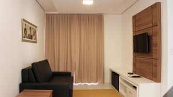 A modern living room with a black sofa, a wooden coffee table, a TV mounted on a wooden cabinet, and a large window with curtains.