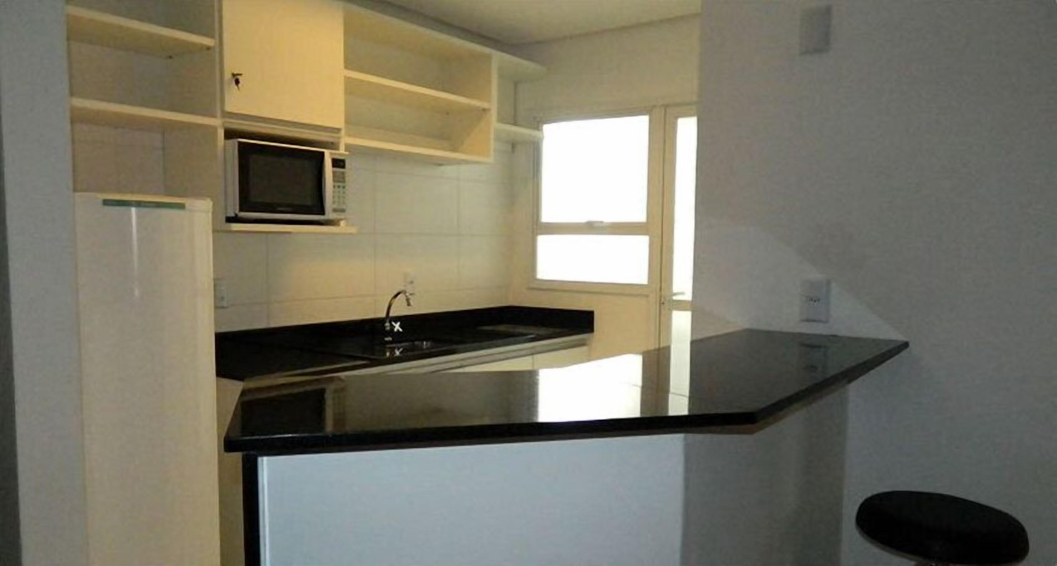 Cozinha com bancada preta, armários brancos, micro-ondas e uma janela.