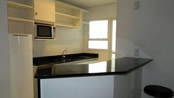 Cozinha com bancada preta, armários brancos, micro-ondas e uma janela.
