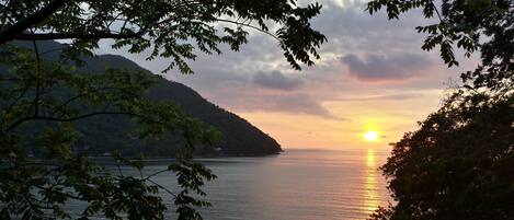 A sunset over a calm body of water with mountains in the background and trees framing the scene.
