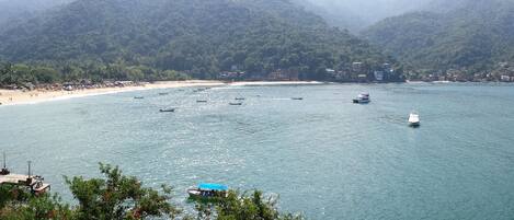 A coastal view with a beach, boats, and mountainous terrain.