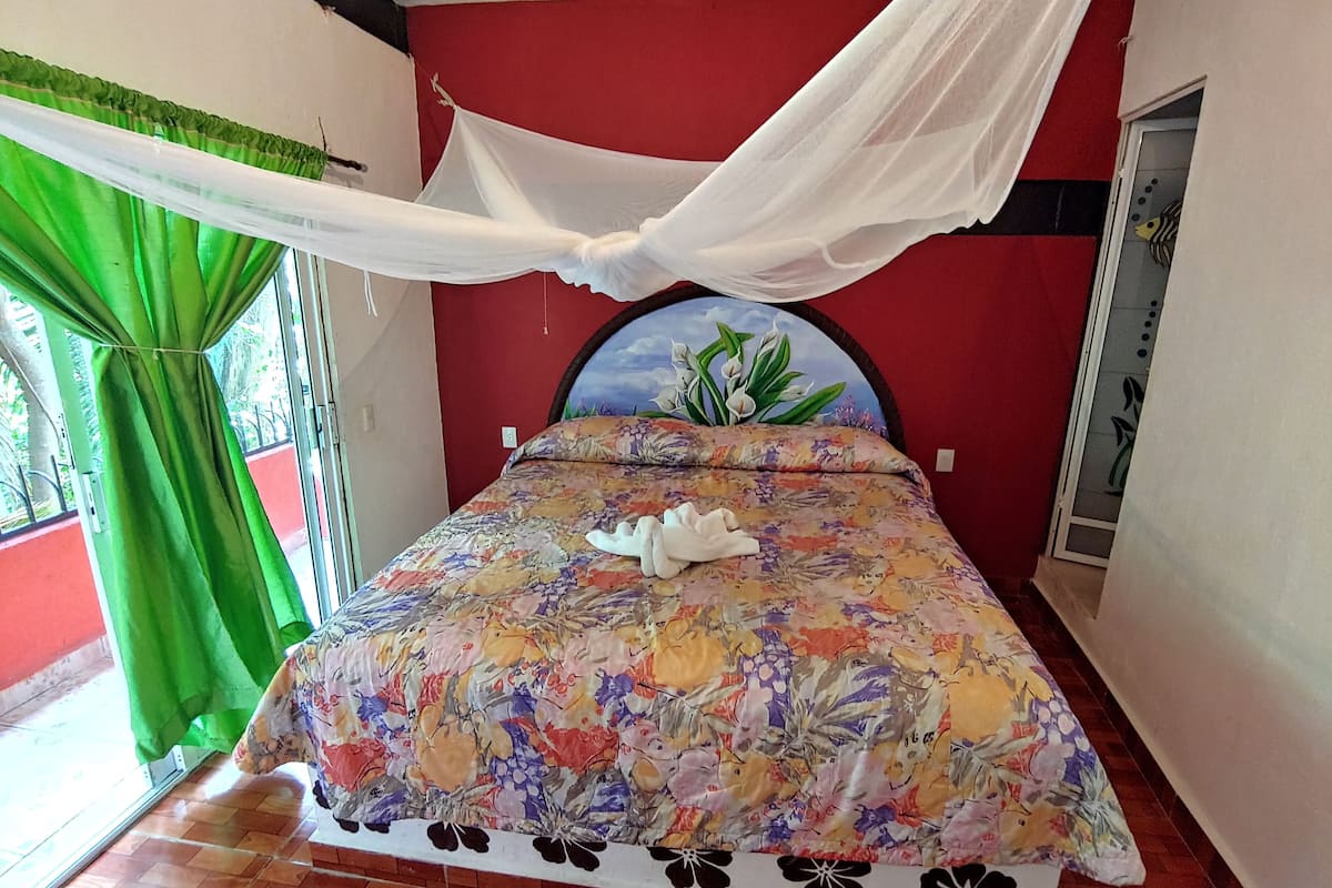 Ein Zimmer mit einem Bett, grünen Vorhängen, einem weißen Baldachin und einer blumigen Tagesdecke.