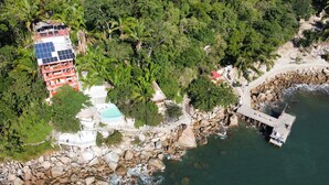 An aerial view of a coastal property with a swimming pool, a dock, and a building with solar panels.