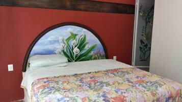 Una cama con una colcha floral, un cabecero con un paisaje pintado y una pared roja.