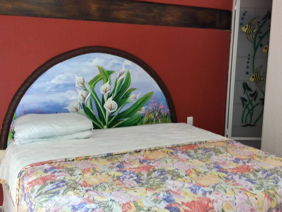 Una cama con una colcha floral, un cabecero con un paisaje pintado y una pared roja.