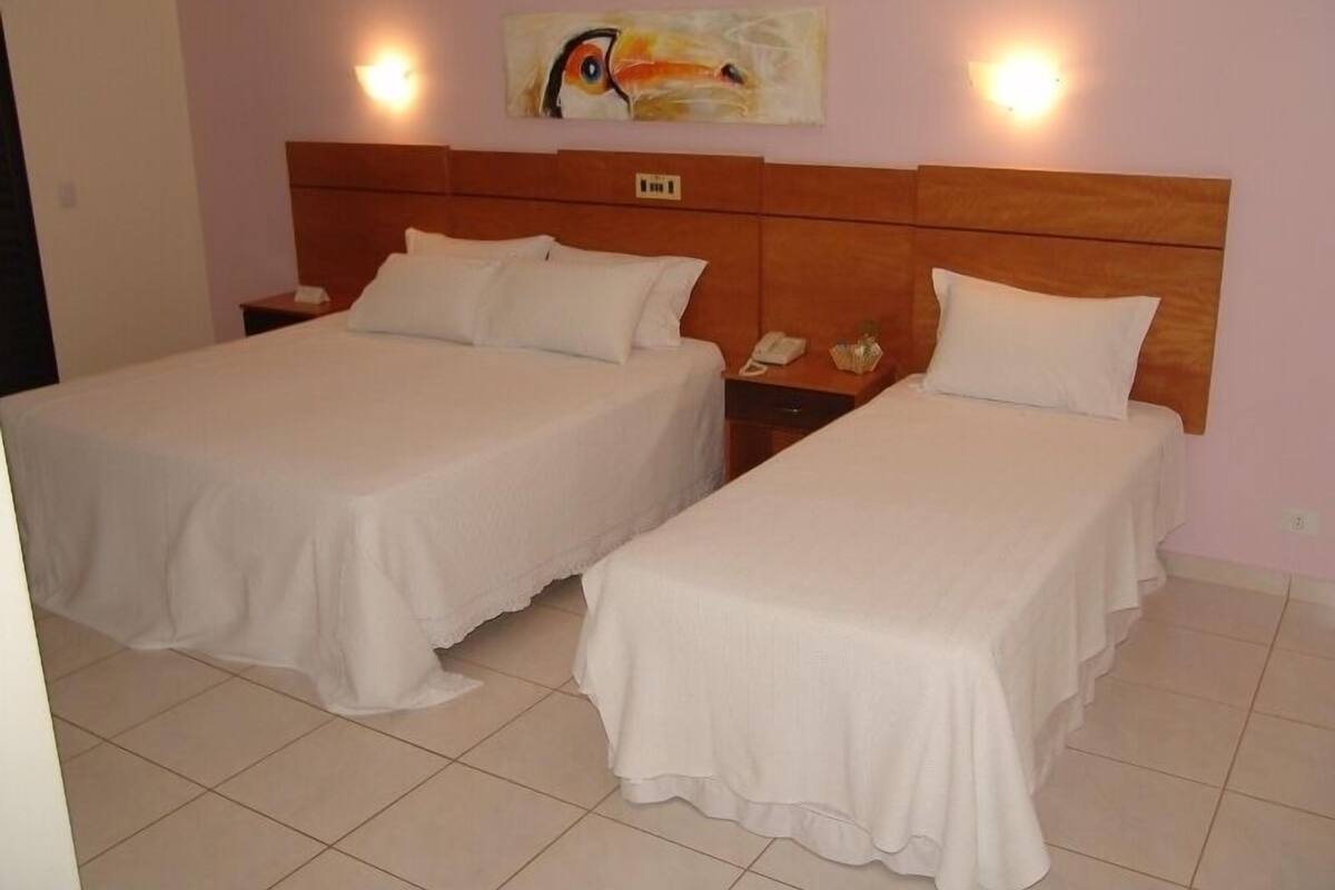 A hotel room with two single beds, a wooden headboard, a painting on the wall, and a bedside table with a phone.