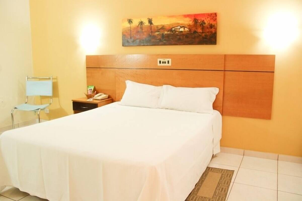 A hotel room with a bed, a nightstand, a chair, and a painting on the wall.