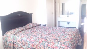 Un lit avec une couvre-lit  à motifs floraux et une tête de lit sombre, dans une chambre d’hôtel.