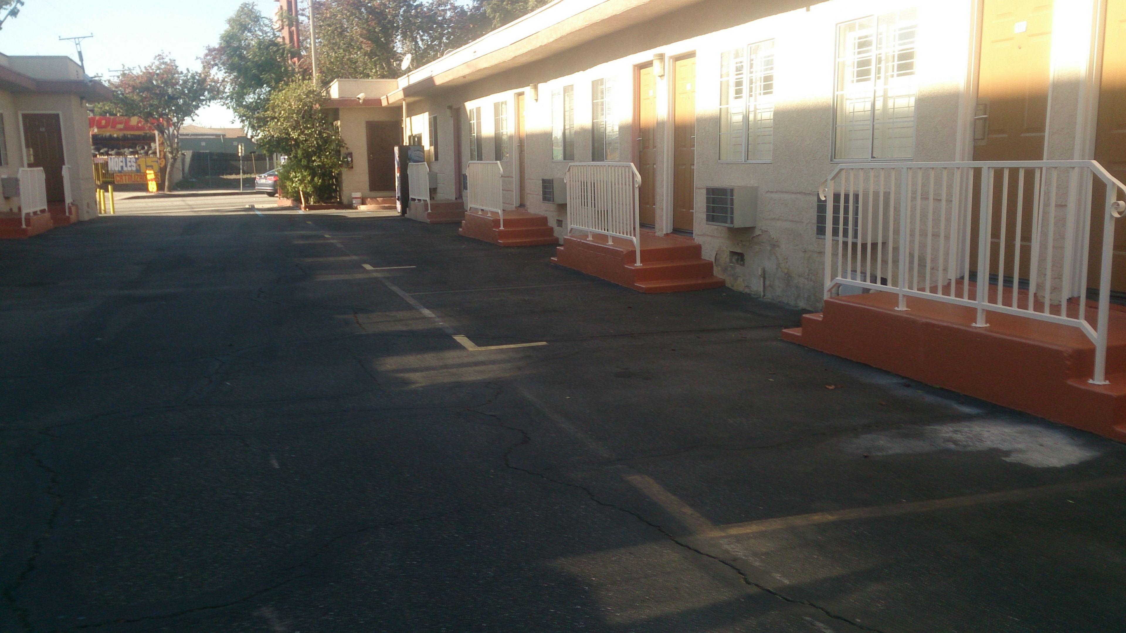 A parking lot with a row of motel-style buildings, each with a single door and a small porch area.