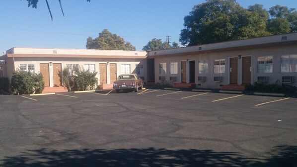 A motel with a parking lot, a parked car, and a building with multiple doors and windows. - Budget Inn (South Gate)