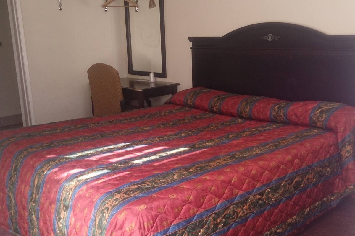 A bedroom with a large bed, a wooden headboard, a bedside table, and a chair.