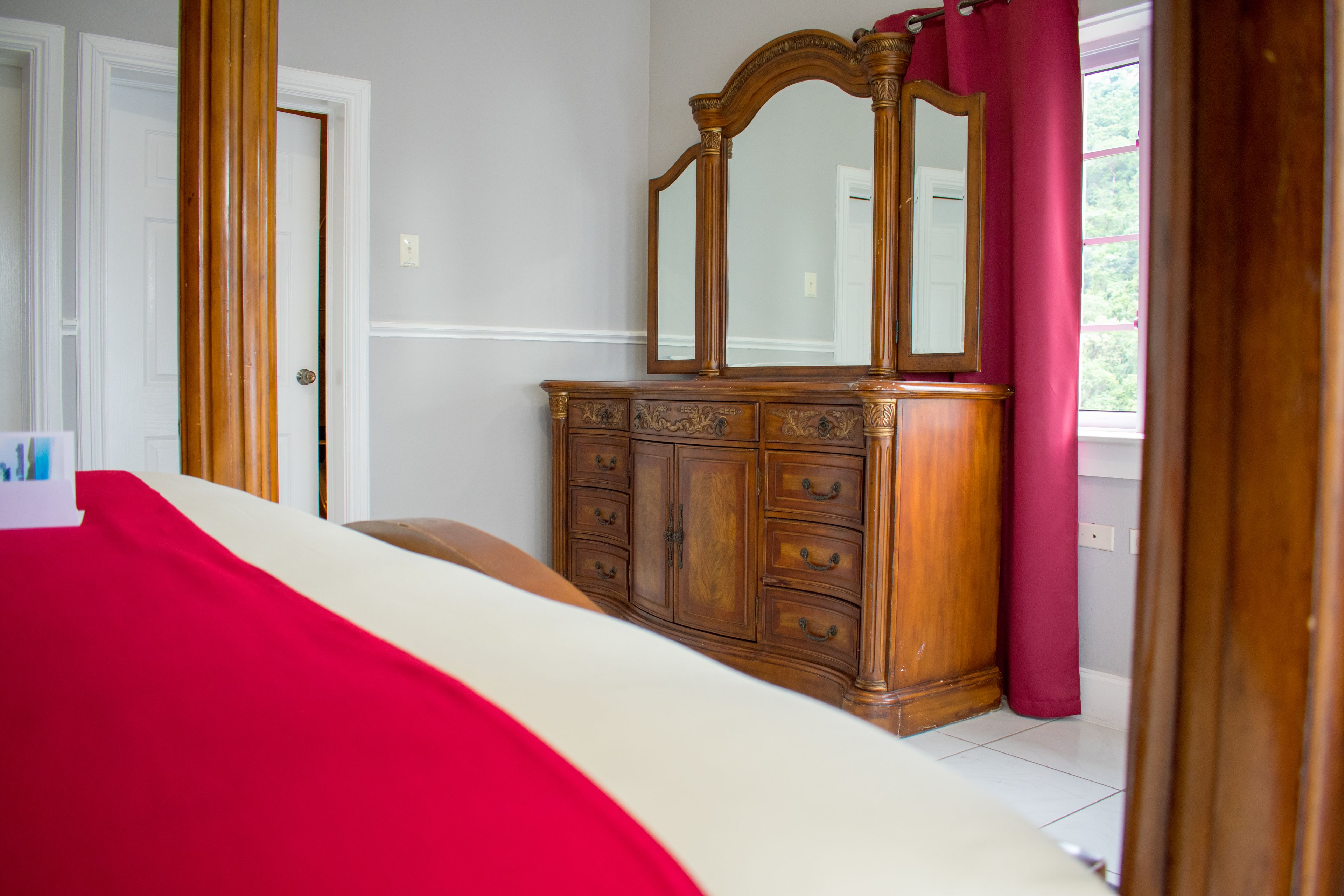 A bedroom with a wooden dresser, a mirror, and a bed with a red blanket.