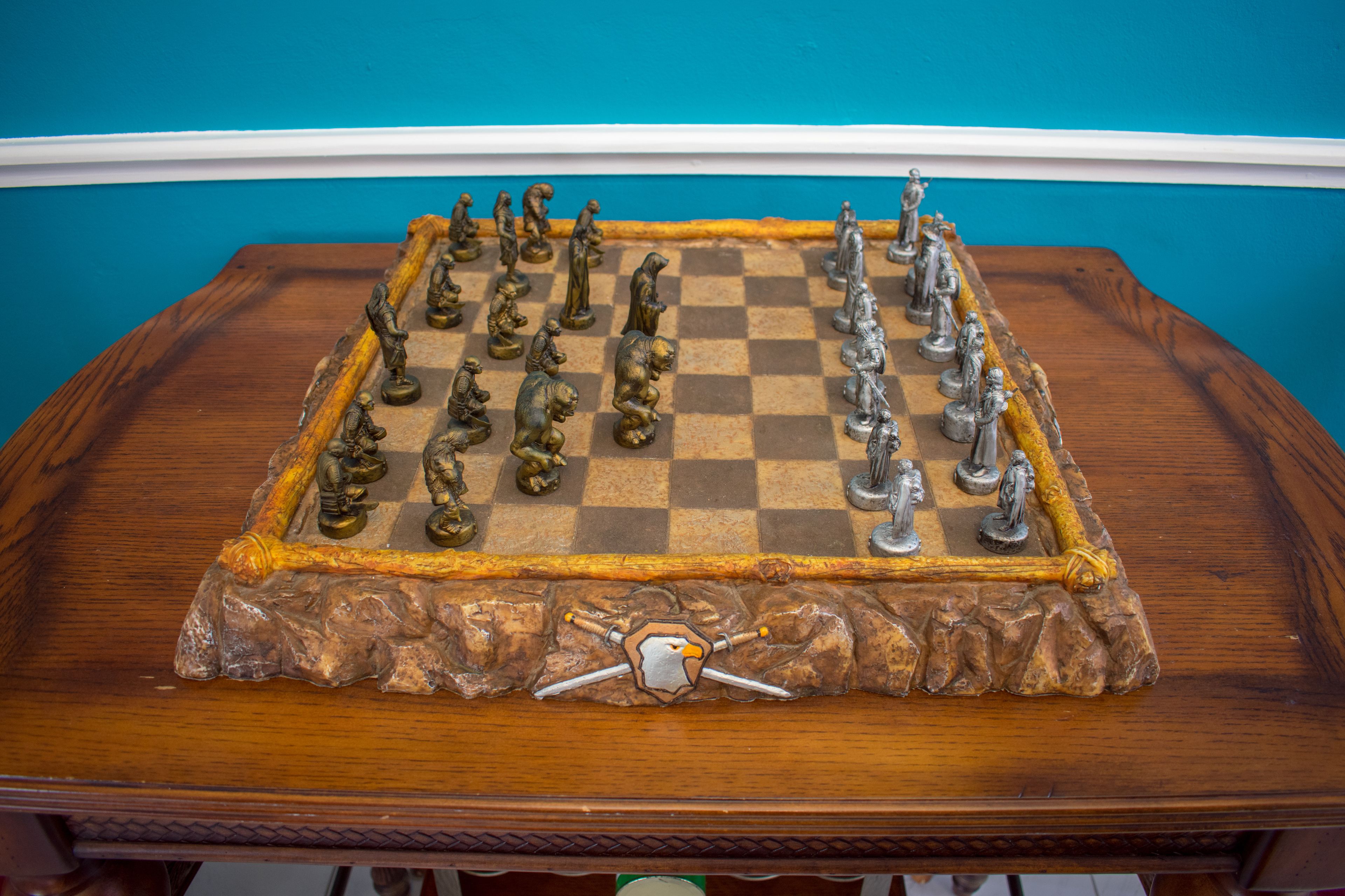 A chessboard with a unique design, placed on a wooden table against a blue wall.