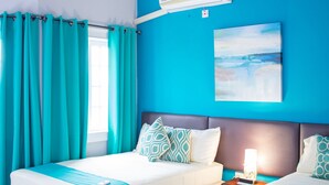 Hotelkamer met twee bedden, blauwgroene gordijnen, een plafondventilator en een wandairconditioner.