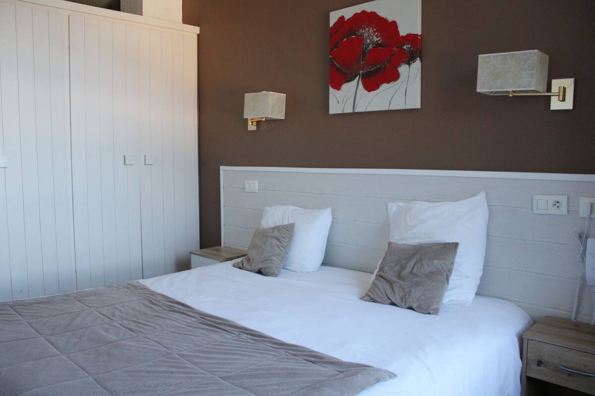 A bedroom with a bed, two bedside tables, a nightstand, a wall-mounted lamp, and a painting.