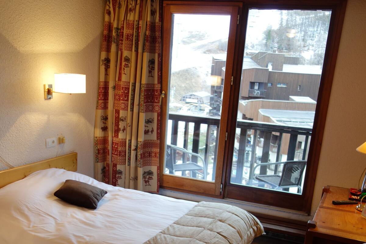 A hotel room with two beds, a desk, and a view of a balcony with buildings.