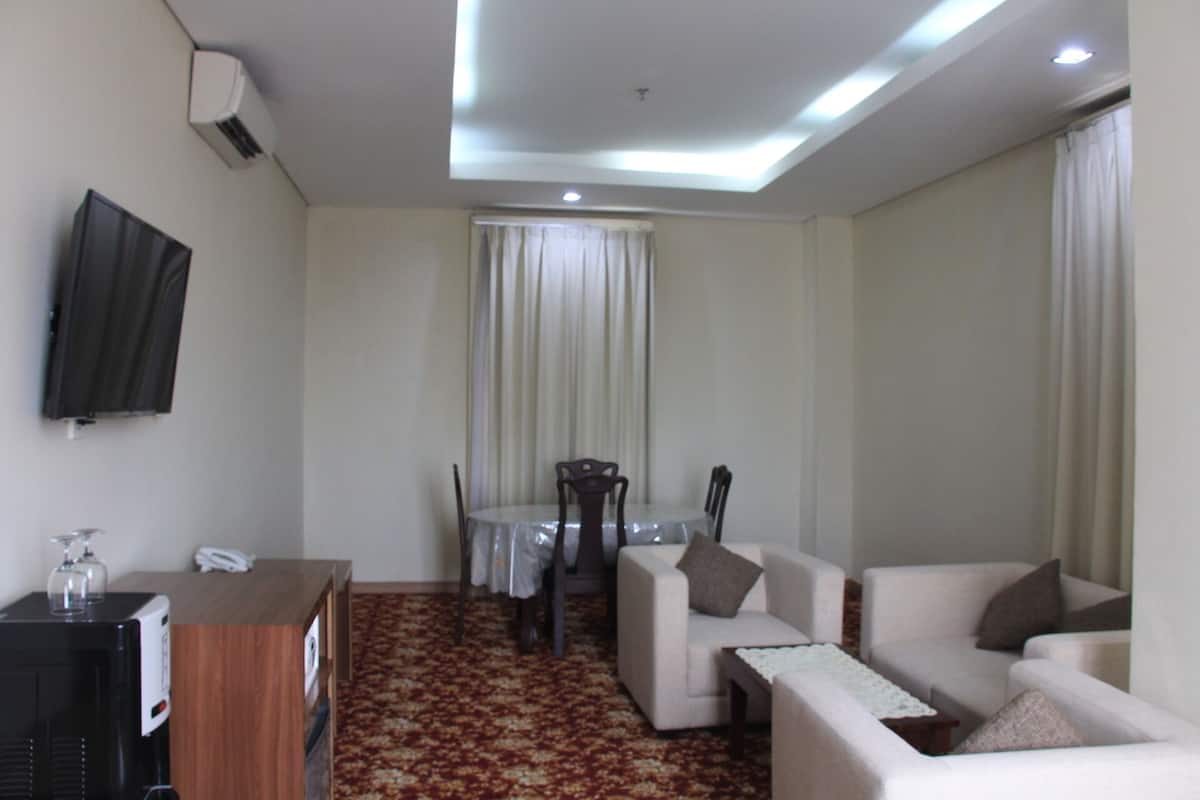 A modern living room with a flat-screen TV mounted on the wall, a dining table with chairs, and a sofa.