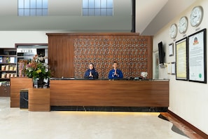 A reception desk with two staff members, a clock, and a wall with framed certificates. - Hotel Namira Syariah Pekalongan (Pekalongan)