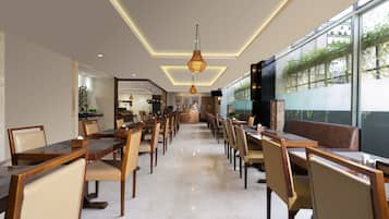 A spacious dining area with multiple tables and chairs, a modern chandelier, and large windows offering a view of greenery outside.