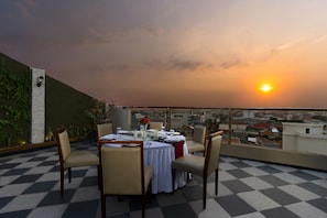 A dining table set for four with chairs, a view of the cityscape, and a sunset in the background. - Hotel Namira Syariah Pekalongan (Pekalongan)