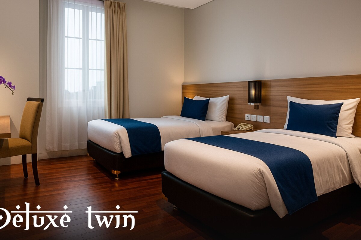 A hotel room with two beds, a desk with a laptop, a TV, and a window with curtains.