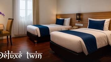 Quarto de hotel com duas camas, uma escrivaninha com um laptop, uma televisão e uma janela com cortinas.