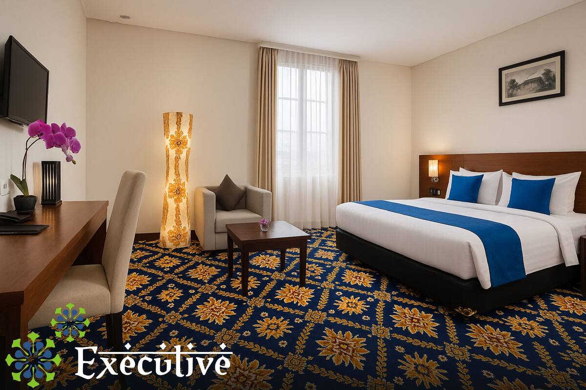 A hotel room with a bed, a desk, a chair, a lamp, and a large window with curtains.