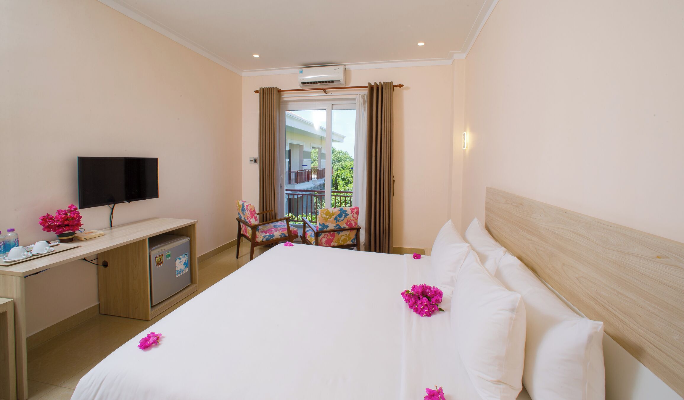Une chambre d’hôtel avec un lit, un bureau avec une télévision, un petit réfrigérateur et un balcon avec vue.
