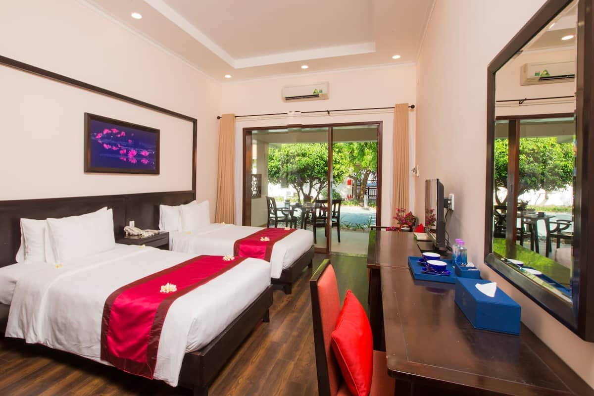 A hotel room with two beds, a dining table, chairs, a TV, and a view of the outdoors.