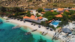 An aerial view of a coastal resort with multiple buildings, a beach, and clear turquoise waters.