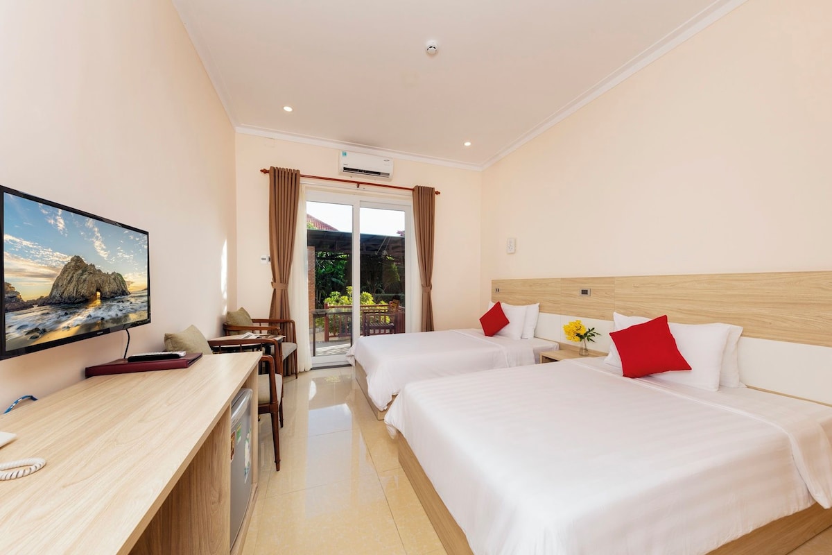 A hotel room with two beds, a desk, a television, and a sliding glass door to the outside.