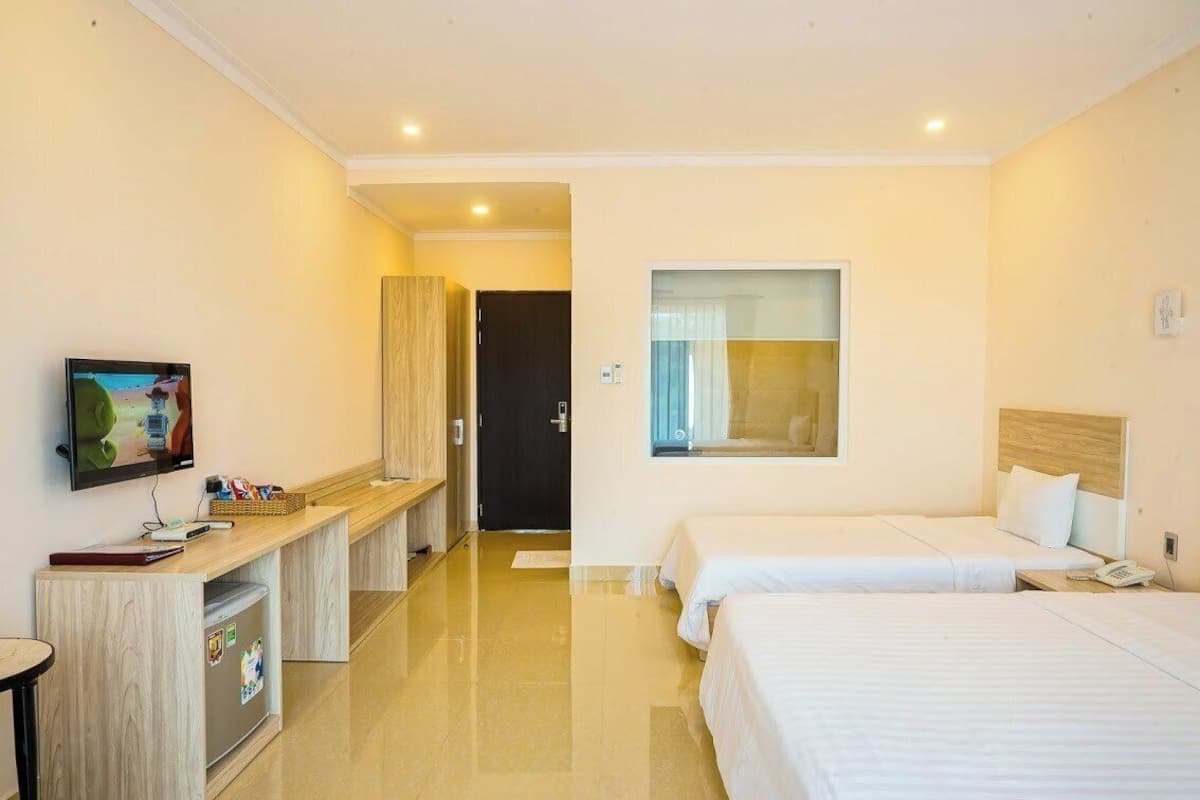 A hotel room with two beds, a desk with a computer, a television, and a window with curtains.