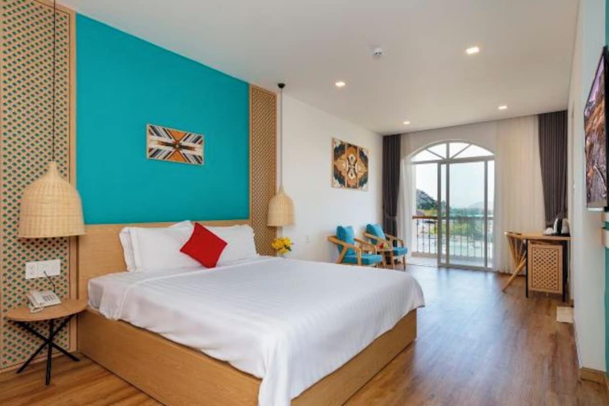 A modern hotel room with a large bed, a desk, and a balcony with a view.