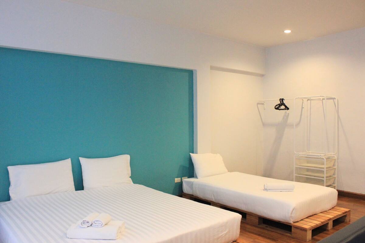 A hotel room with two beds, a teal accent wall, and a white hanging rack.