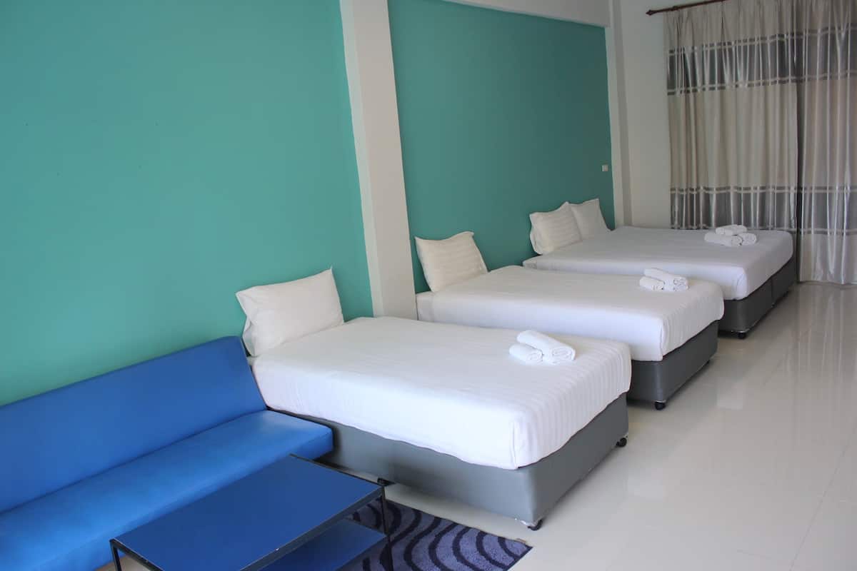 A hotel room with three single beds, a blue sofa, and a small table.