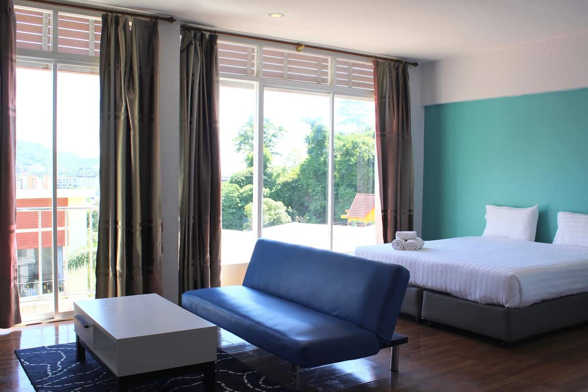 A hotel room with a bed, a sofa, a small table, and a view of the outdoors.