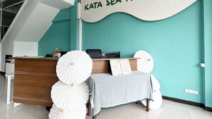 A reception area with a desk, a sign that reads "KATA SEA HOST," and a ceiling fan. - Kata Sea Boutique (Karon)