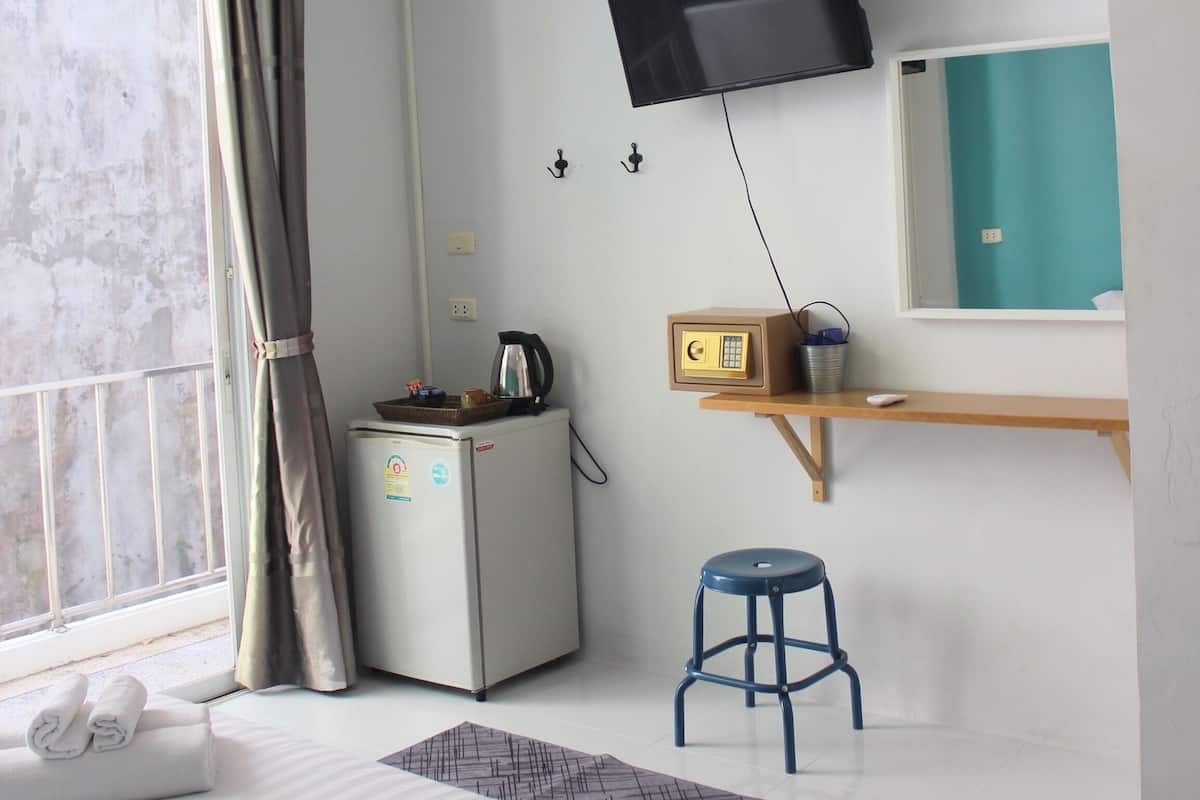 A hotel room with a bed, a desk with a computer, a small refrigerator, a TV mounted on the wall, and a window with curtains.