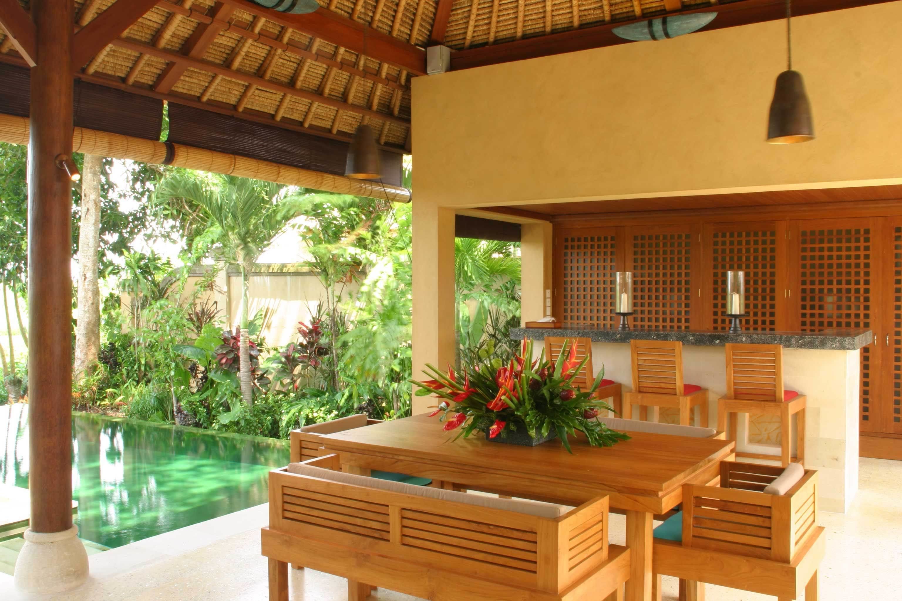 A wooden dining table with chairs, a flower centerpiece, and a kitchen area with a counter and cabinets.