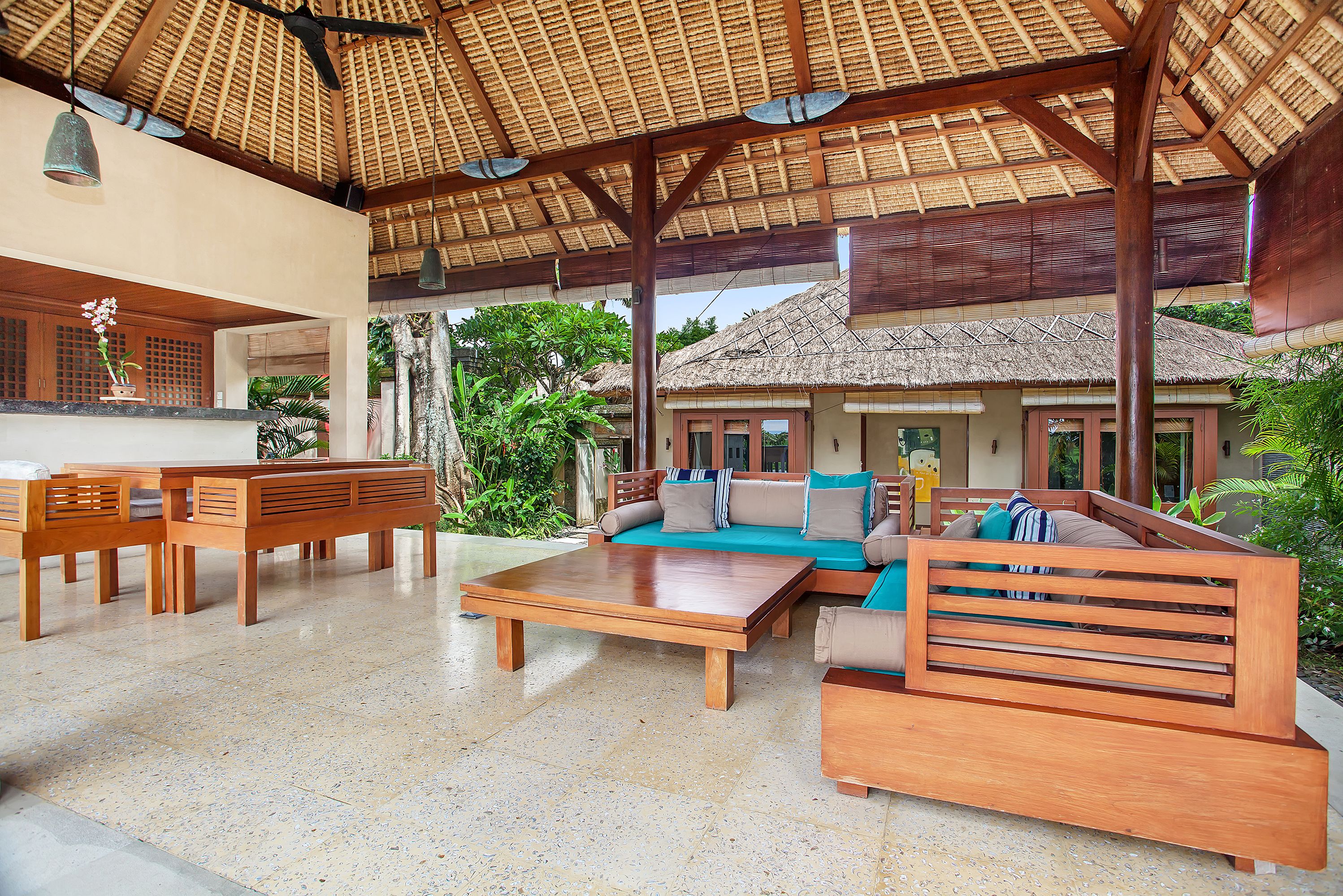 A spacious indoor area with a thatched roof, wooden furniture, and a view of a house with a thatched roof.