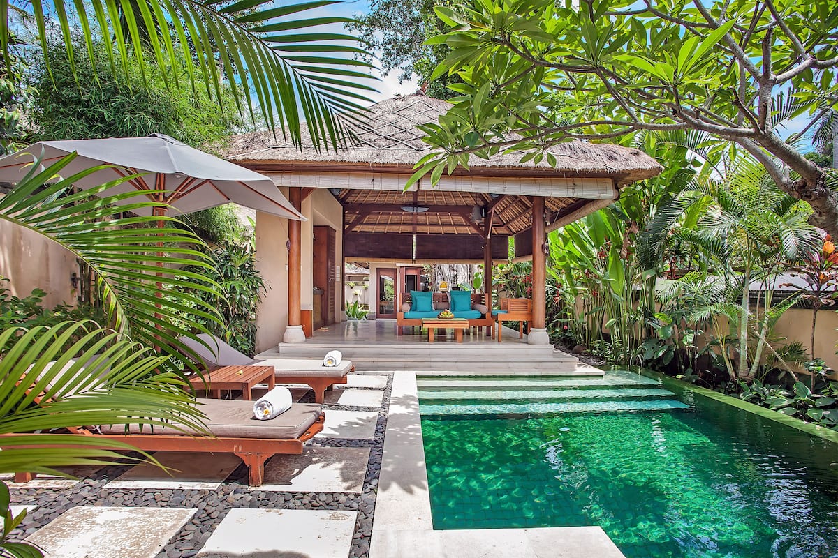 A pool area with lounge chairs and umbrellas, surrounded by lush greenery.