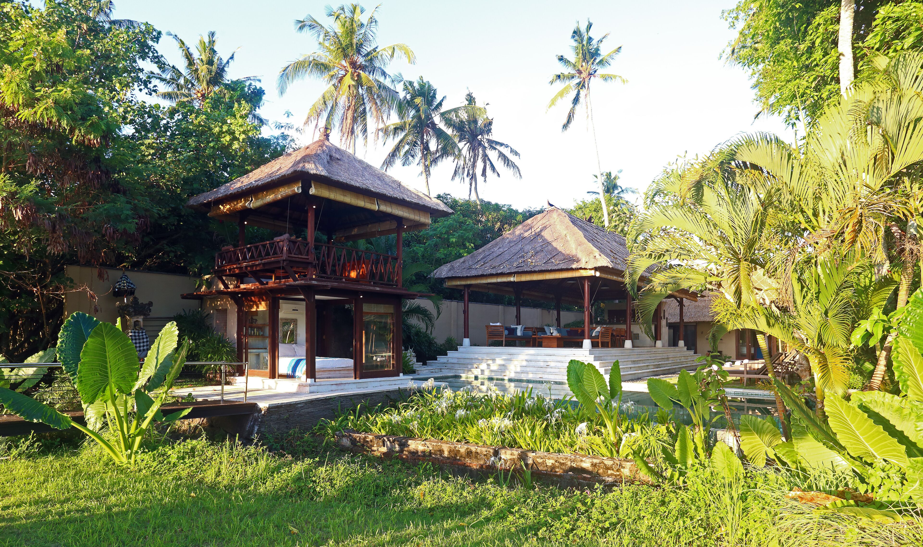 A tropical resort with thatched-roof structures, a pool, and lush greenery.
